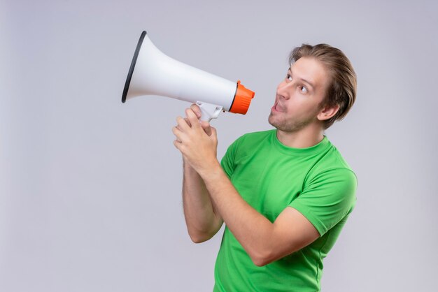 Jeune bel homme portant un t-shirt vert criant au mégaphone