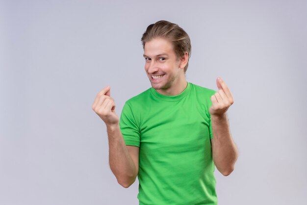 Jeune bel homme portant un t-shirt vert faisant un geste d'argent