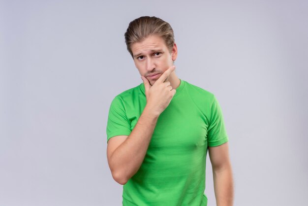 Jeune bel homme portant un t-shirt vert avec la main sur le menton