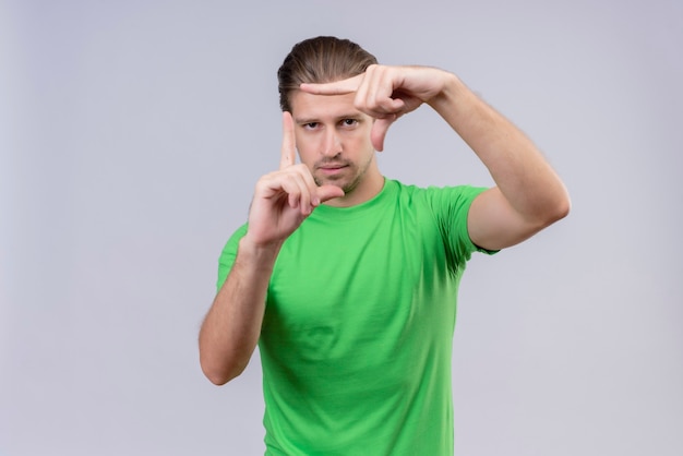 Jeune bel homme portant un t-shirt vert regardant à travers un cadre formé par ses mains