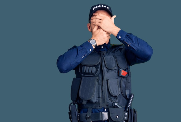 Jeune bel homme portant un uniforme de police couvrant les yeux et la bouche avec les mains surpris et choqué cachant l'émotion