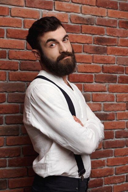 Jeune bel homme posant avec les bras croisés sur le mur de briques.