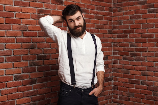 Jeune bel homme posant sur le mur de briques.