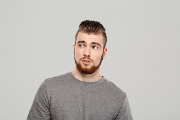 Jeune bel homme posant sur un mur gris.