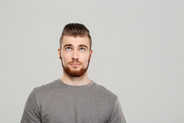 Jeune bel homme posant sur un mur gris.