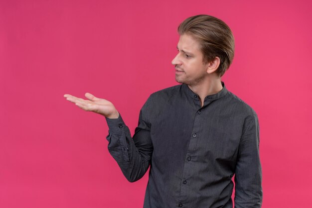 Jeune bel homme présentant un espace copie avec le bras de sa main debout sur un mur rose