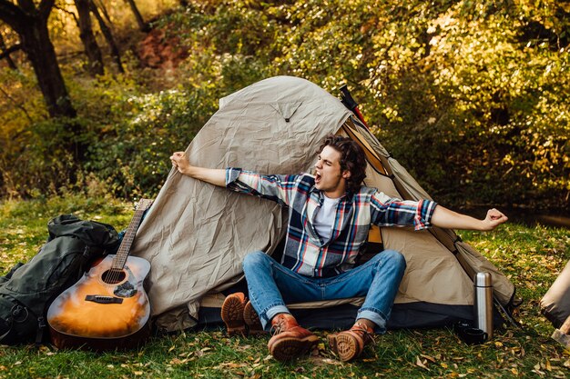 Jeune bel homme s'étend le matin près de la tente dans le camping dans la nature