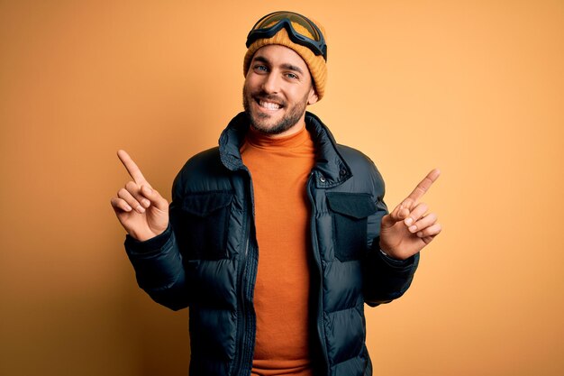 Jeune bel homme skieur avec barbe portant des vêtements de sport de neige et des lunettes de ski souriant confiant pointant avec les doigts vers différentes directions Copier l'espace pour la publicité