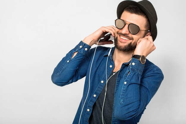 Jeune bel homme souriant heureux écoutant de la musique dans des écouteurs isolés sur le mur blanc du studio