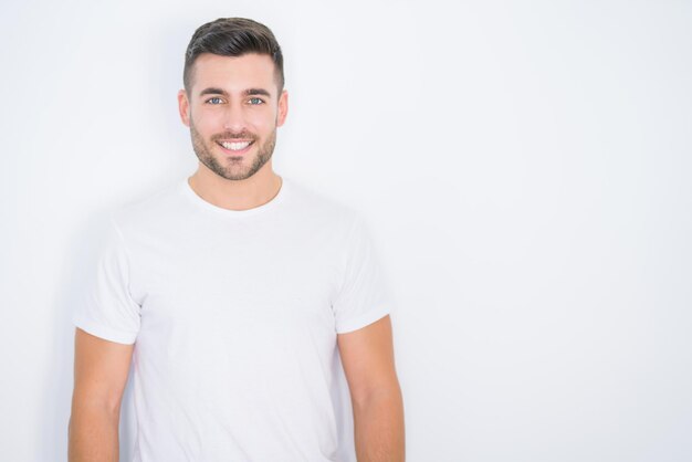 Jeune bel homme souriant heureux portant un t-shirt blanc décontracté sur fond isolé blanc