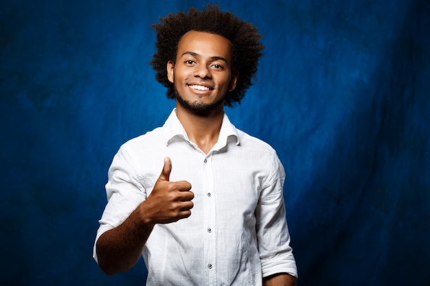 Jeune bel homme souriant, montrant bien sur la surface bleue