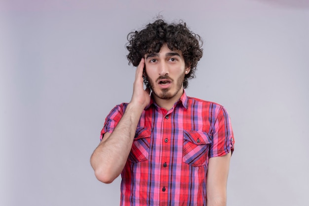 Photo gratuite un jeune bel homme surpris aux cheveux bouclés en chemise à carreaux en gardant la tête sur la tête