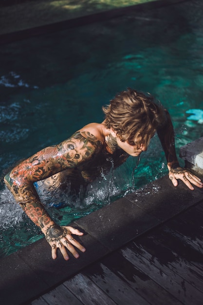 jeune bel homme en tatouages ​​reposant dans la piscine extérieure.