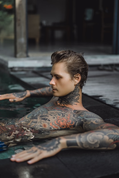 Photo gratuite jeune bel homme en tatouages ​​reposant dans la piscine extérieure.