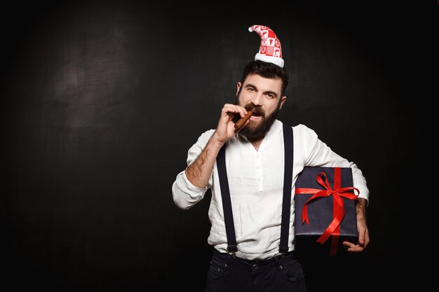 Jeune bel homme tenant une boîte-cadeau de Noël sur fond noir.