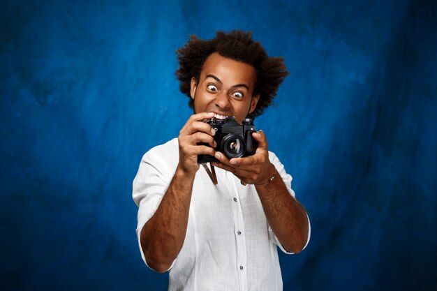 Jeune bel homme tenant un vieil appareil photo sur une surface bleue