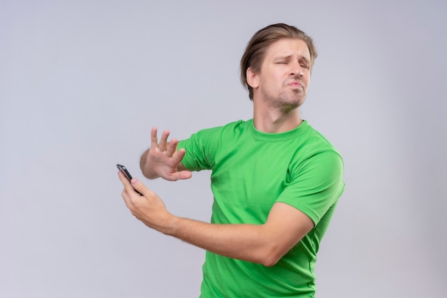 Jeune bel homme vêtu d'un t-shirt vert debout sur un mur blanc