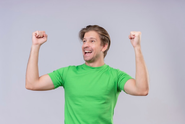 Jeune bel homme vêtu d'un t-shirt vert, excité et heureux, serrant les poings