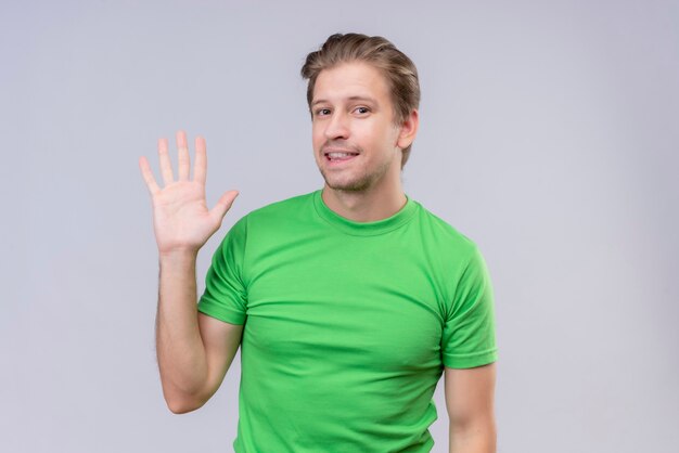 Jeune bel homme vêtu d'un t-shirt vert à la recherche et souriant confiden