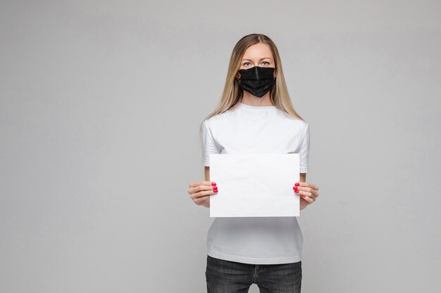 Jeune belle adolescente caucasienne en t-shirt blanc, jeans se dresse avec un masque médical noir détient un grand écran blanc