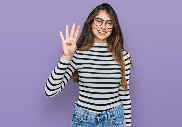 Jeune belle adolescente portant des vêtements décontractés et des lunettes montrant et pointant vers le haut avec les doigts numéro quatre tout en souriant confiant et heureux