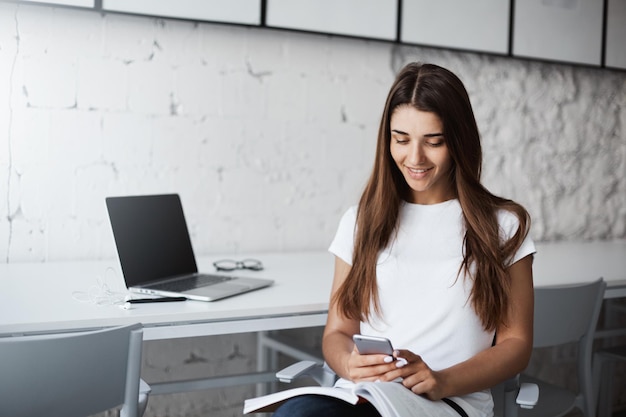 Jeune belle dame heureuse à l'aide d'un téléphone intelligent pour apprendre une nouvelle langue dans un café lumineux Concept d'éducation