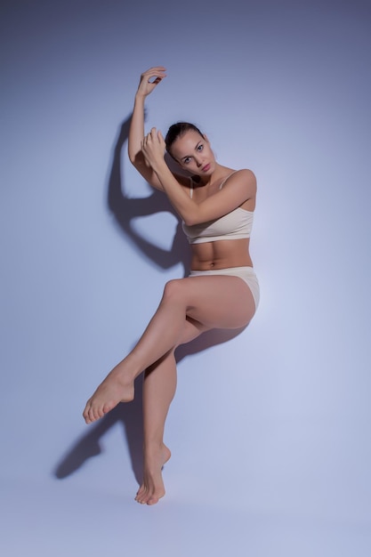 Jeune belle danseuse en maillot de bain beige dansant sur studio lilas