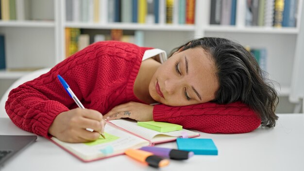 Photo gratuite jeune belle étudiante hispanique écrivant des notes fatiguées à l'université de bibliothèque