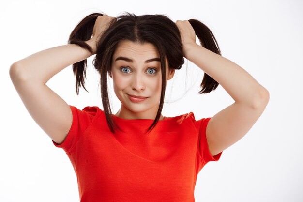 Jeune belle femme d'affaires brune en colère folle serrant la tête et hurlant en regardant loin sur le mur blanc