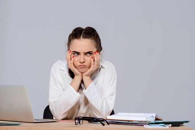 Jeune belle femme d'affaires mécontent assis sur le lieu de travail sur le mur violet