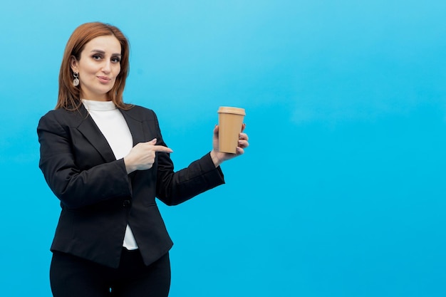 Jeune belle femme d'affaires tenant une tasse de café et pointant du doigt dessus