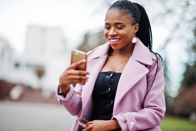 Jeune belle femme afro-américaine élégante dans la rue portant un manteau de tenue de mode avec un téléphone portable