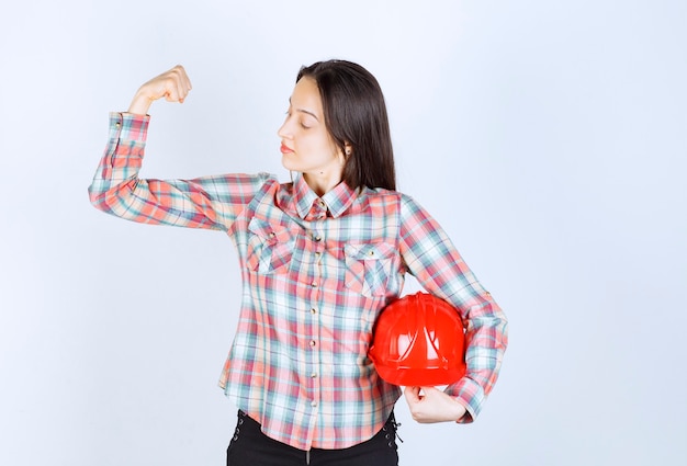 Jeune belle femme architecte tenant un casque de sécurité sur un mur blanc.