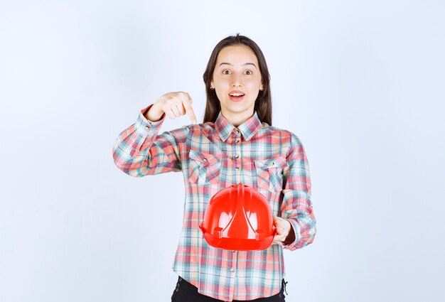 Jeune belle femme architecte tenant un casque de sécurité sur un mur blanc.