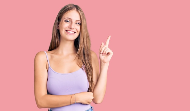 Jeune belle femme blonde portant un style décontracté avec une chemise sans manches souriante heureuse pointant avec la main et le doigt sur le côté