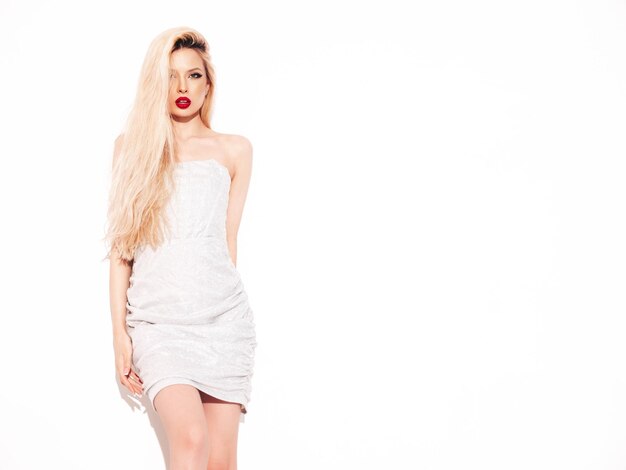 Jeune belle femme confiante en robe argentée de soirée d'été à la mode Sexy femme blonde insouciante posant près d'un mur blanc en studio Modèle avec des lèvres rouges Isolé