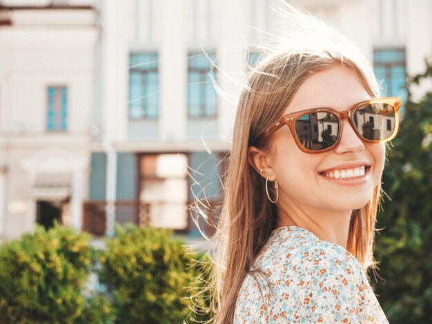 Jeune belle femme hipster souriante dans des vêtements d'été à la mode Sexy femme insouciante posant sur le fond de la rue au coucher du soleil Modèle positif à l'extérieur Gai et heureux en lunettes de soleil