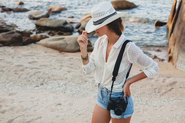 Photo gratuite jeune belle femme hipster en vacances d'été en asie, détente sur la plage tropicale, appareil photo numérique, style boho décontracté, paysage de mer, corps bronzé mince, voyage seul