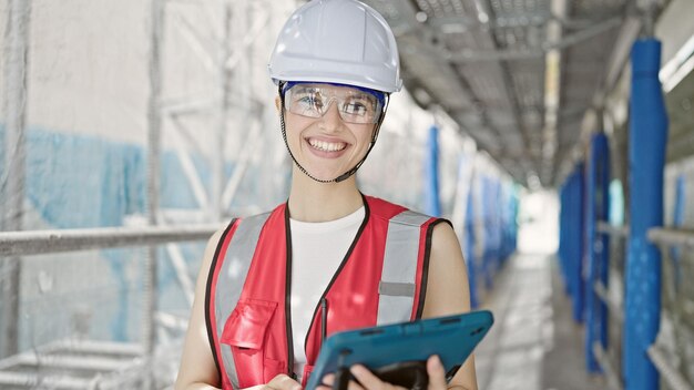 Jeune belle femme hispanique constructeur souriante confiante à l'aide du pavé tactile dans la rue