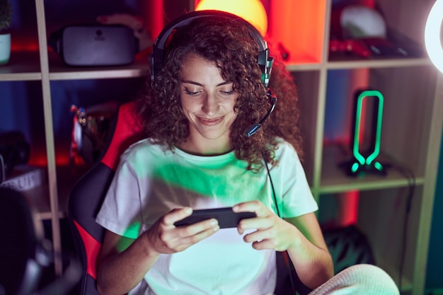 Photo gratuite jeune belle femme hispanique streamer jouant au jeu vidéo à l'aide d'un smartphone dans la salle de jeux