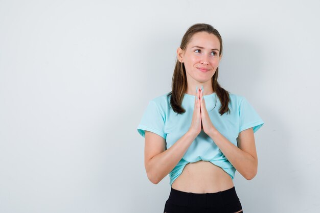 Jeune belle femme avec les mains en geste de prière en t-shirt et à l'air plein d'espoir. vue de face.