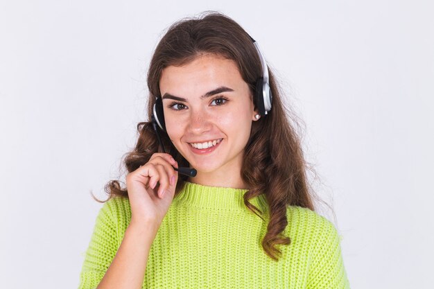 Jeune belle femme avec un maquillage léger de taches de rousseur en pull sur un mur blanc avec un casque d'assistance téléphonique gestionnaire de centre d'appels sourire heureux
