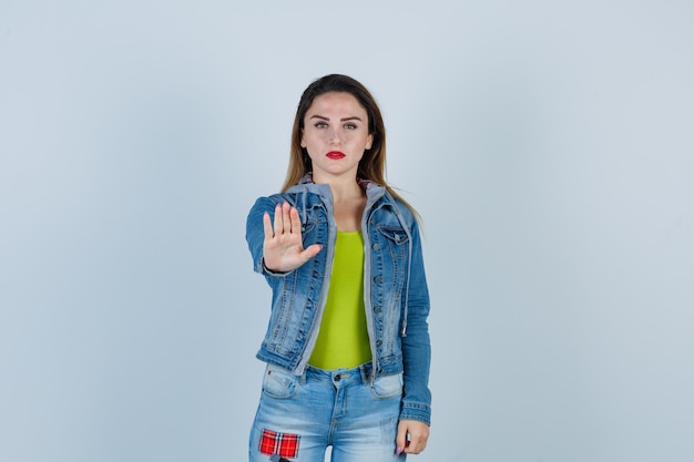 Jeune belle femme montrant un geste d'arrêt en tenue de denim et ayant l'air confiant. vue de face.