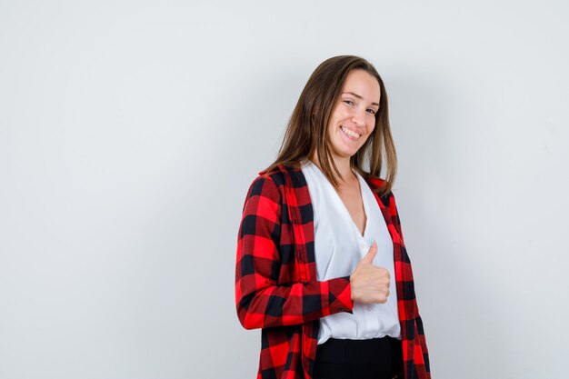 Jeune belle femme montrant le pouce en tenue décontractée et l'air joyeux, vue de face.