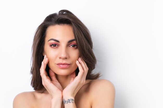 Jeune belle femme avec une peau parfaite maquillage rose printemps lumineux et épaules nues sur fond blanc