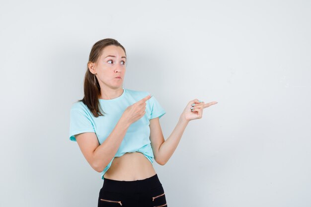 Jeune belle femme pointant vers la droite, regardant de côté en t-shirt, pantalon et l'air terrifiée, vue de face.