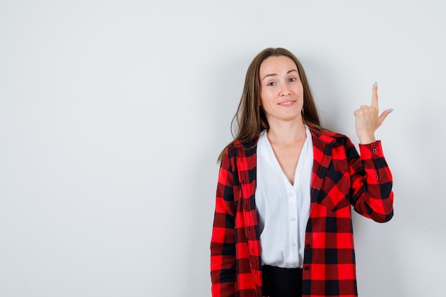 Jeune belle femme pointant vers le haut en tenue décontractée et semblant joyeuse. vue de face.