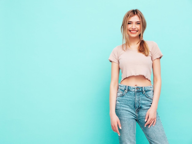 Jeune belle femme souriante dans des vêtements d'été à la mode femme insouciante posant près du mur bleu en studio Modèle brune positive s'amusant Gai et heureux