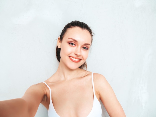 Jeune belle femme souriante en jeans d'été à la mode jupe et haut Sexy femme insouciante posant près d'un mur gris en studio Modèle brune positive s'amusant et devenant fou