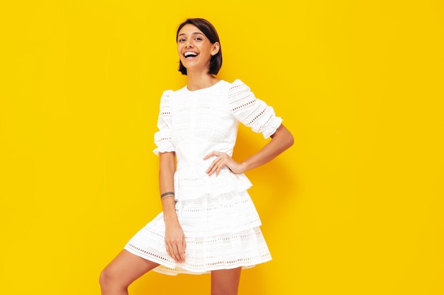 Jeune belle femme souriante en robe blanche d'été à la mode Sexy femme insouciante posant près du mur jaune en studio Modèle positif s'amusant Gai et heureux Isolé